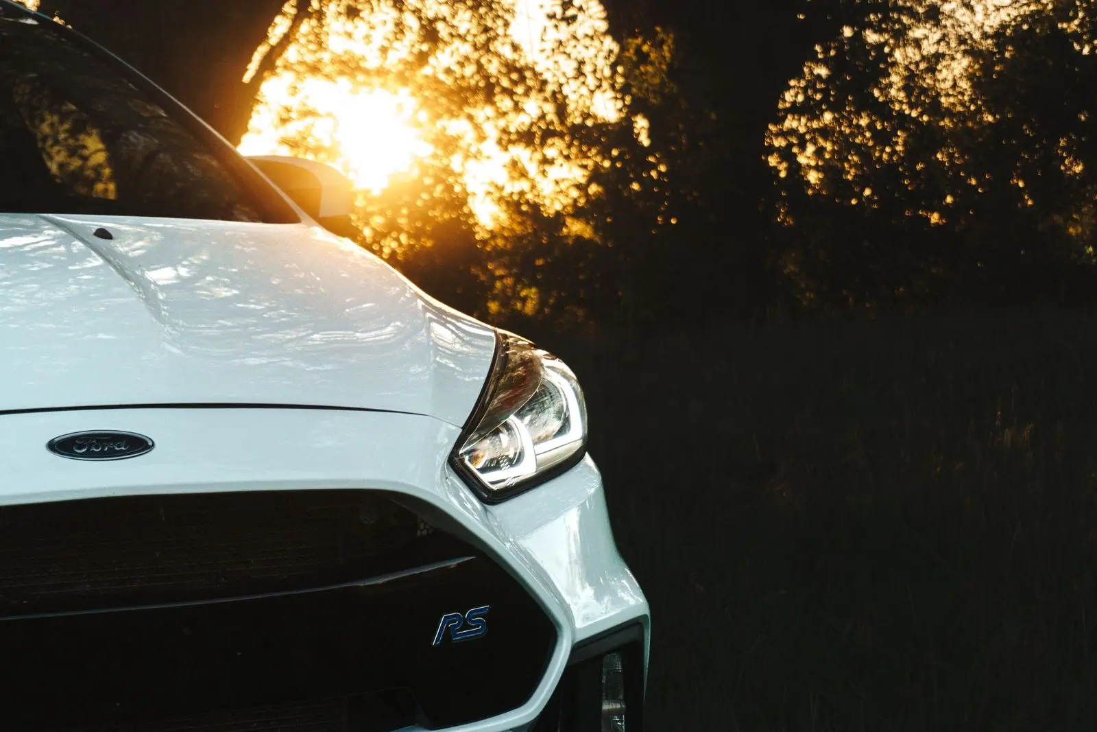 White hatchback headlight and grille detail at sunset